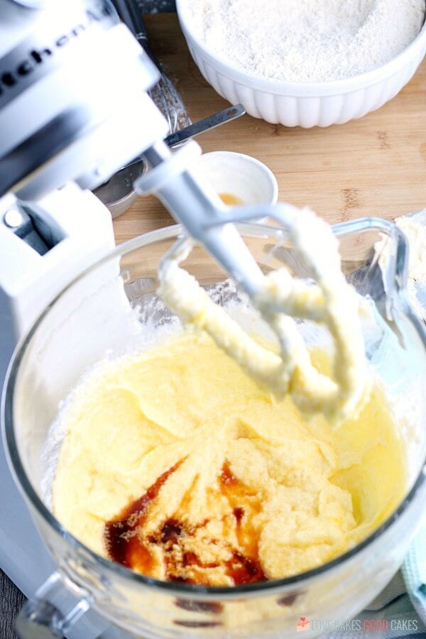 Soft Sugar Cookie dough in an electric mixer bowl with more ingredients being added.