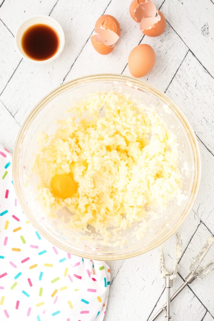 Second egg added to the creamed mixture for soft sugar cookies, with eggshells in the background.