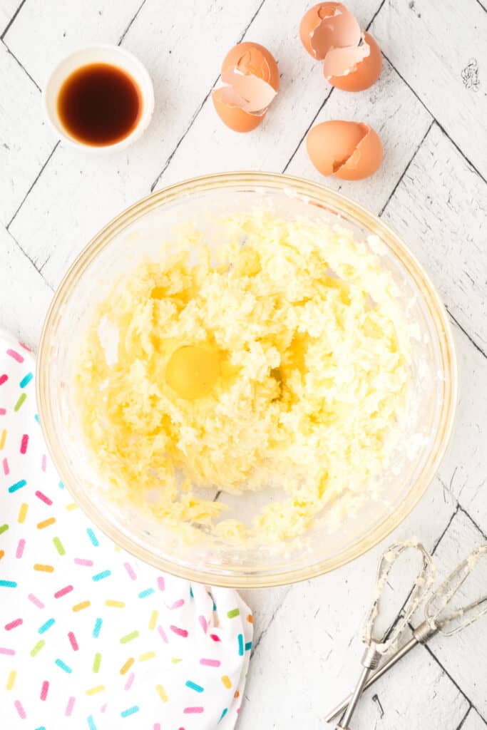 Third egg being mixed into the creamed butter and sugar mixture for cookie dough preparation.