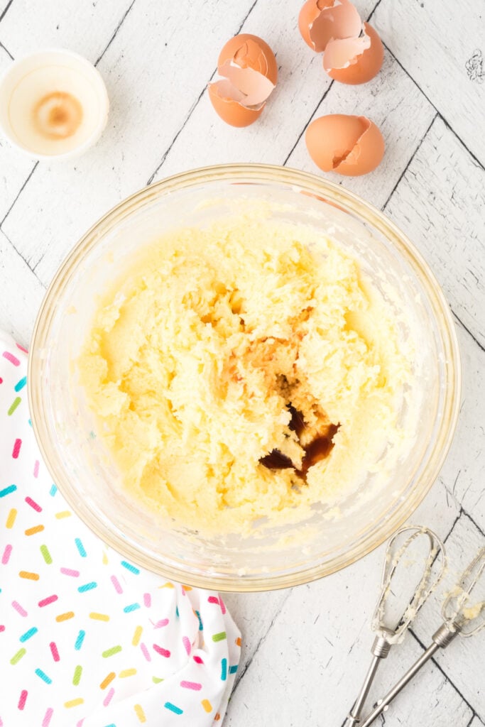 Vanilla extract added to the creamed butter, sugar, and egg mixture in a clear bowl.