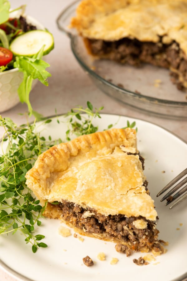 Canadian Meat Pie slice on plate with rest of pie in background