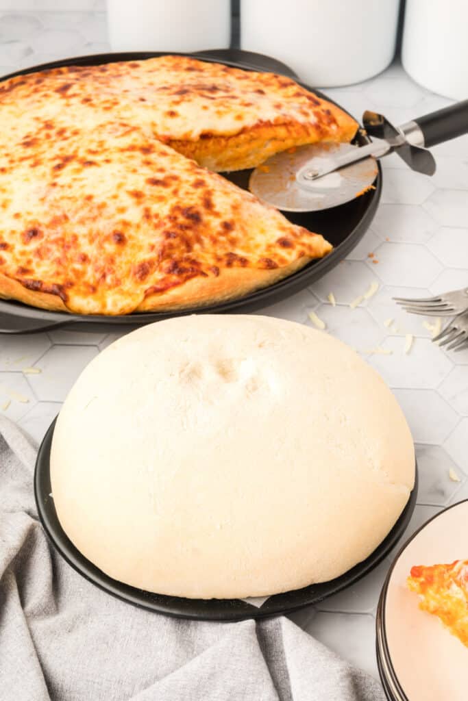Homemade cheese pizza made with Bread Machine Pizza Dough beside an extra prepared pizza crust