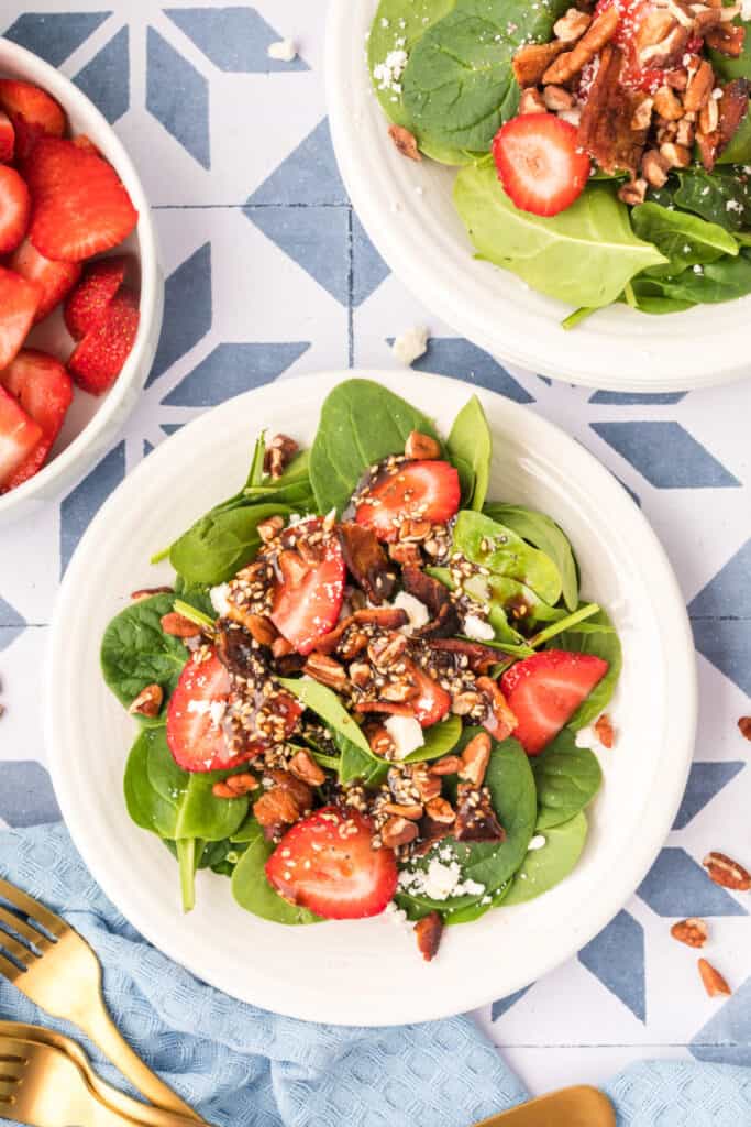 finished strawberry spinach salad with balsamic poppy seed dressing, bacon, feta, pecans, and strawberries on a plate