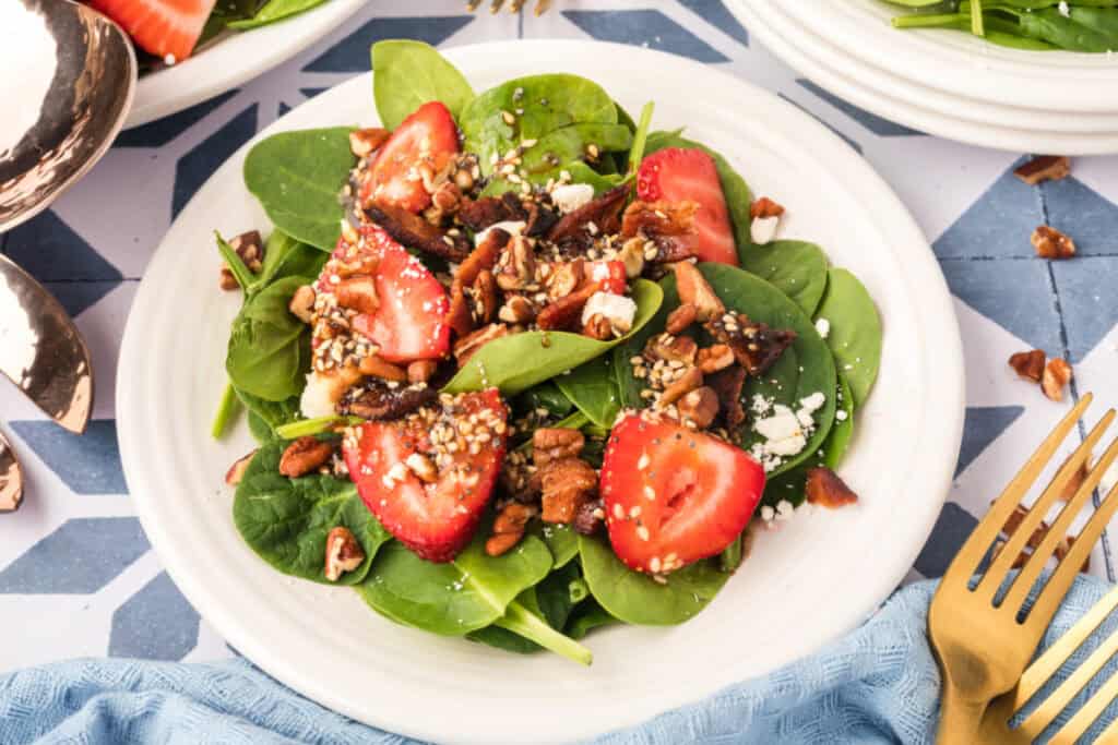 close-up of strawberry spinach salad with balsamic poppy seed dressing, bacon, feta, pecans, and sliced strawberries on a plate