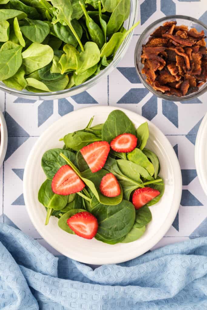 spinach leaves on a plate topped with sliced strawberries for strawberry spinach salad