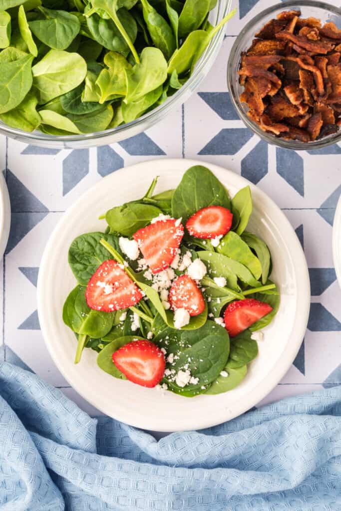 spinach and strawberries topped with crumbled feta cheese on a plate for strawberry spinach salad