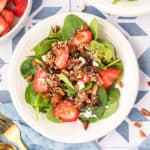 square image of strawberry spinach salad with balsamic poppy seed dressing, bacon, feta, pecans, and sliced strawberries on a plate