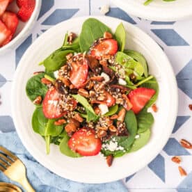 square image of strawberry spinach salad with balsamic poppy seed dressing, bacon, feta, pecans, and sliced strawberries on a plate