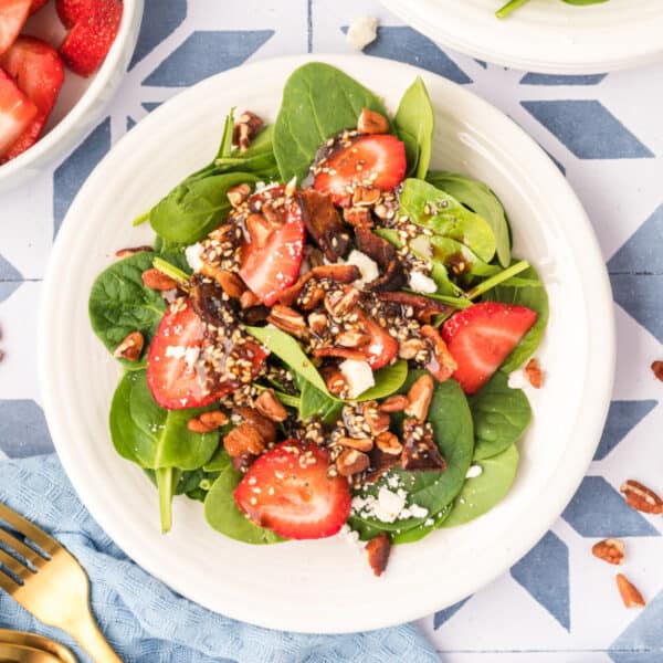 square image of strawberry spinach salad with balsamic poppy seed dressing, bacon, feta, pecans, and sliced strawberries on a plate