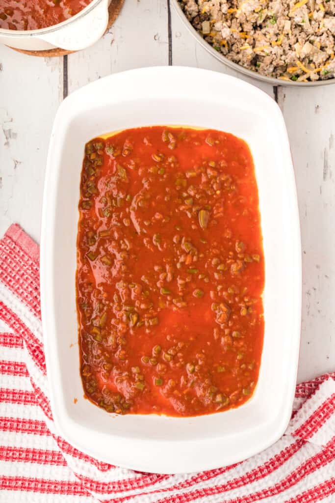 baking dish with enchilada sauce spread across the bottom ready for layering