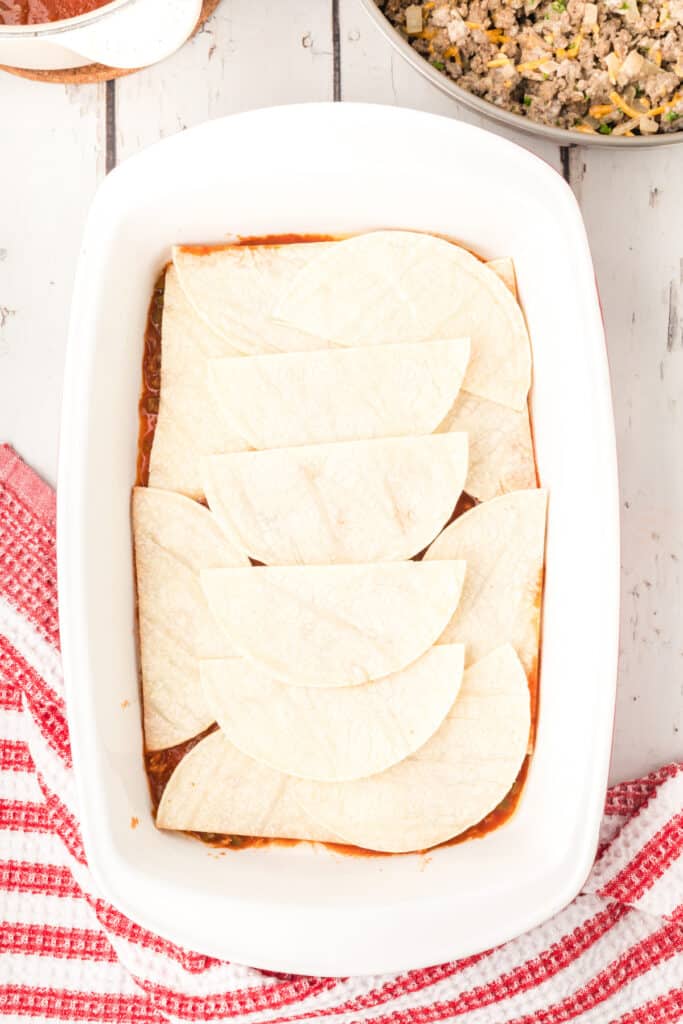 corn tortillas layered in a baking dish over enchilada sauce