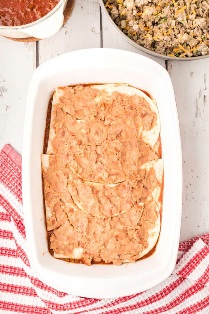 refried beans spread over tortillas in a baking dish
