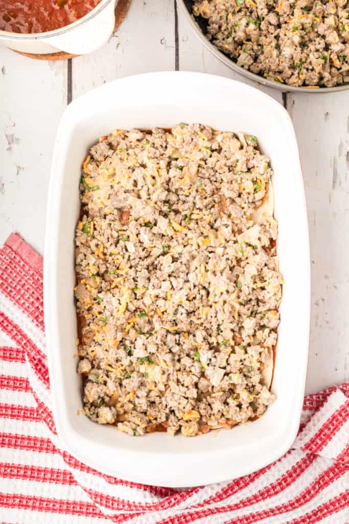 beef mixture spread over refried beans in a baking dish