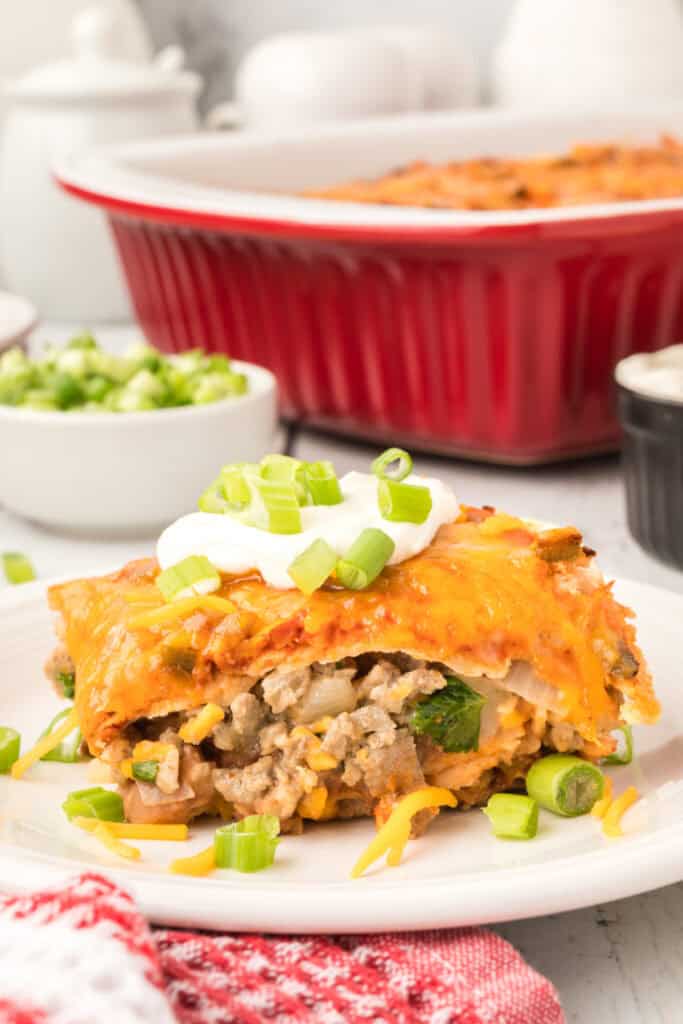 beef and bean enchilada casserole served on a plate with sour cream and green onions