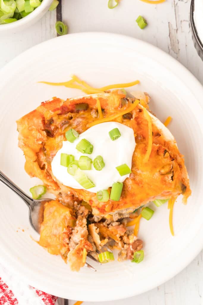 plated beef and bean enchilada casserole with a bite taken out topped with sour cream and green onions