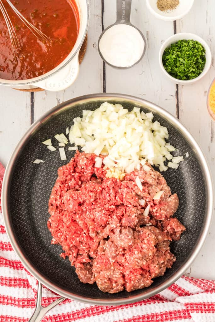 ground beef and chopped onions cooking in a skillet before browning