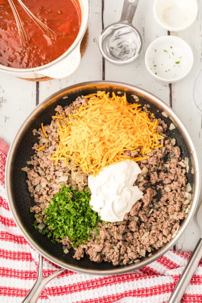 cooked beef mixture with sour cream, cheese, parsley, and seasoning added in a skillet