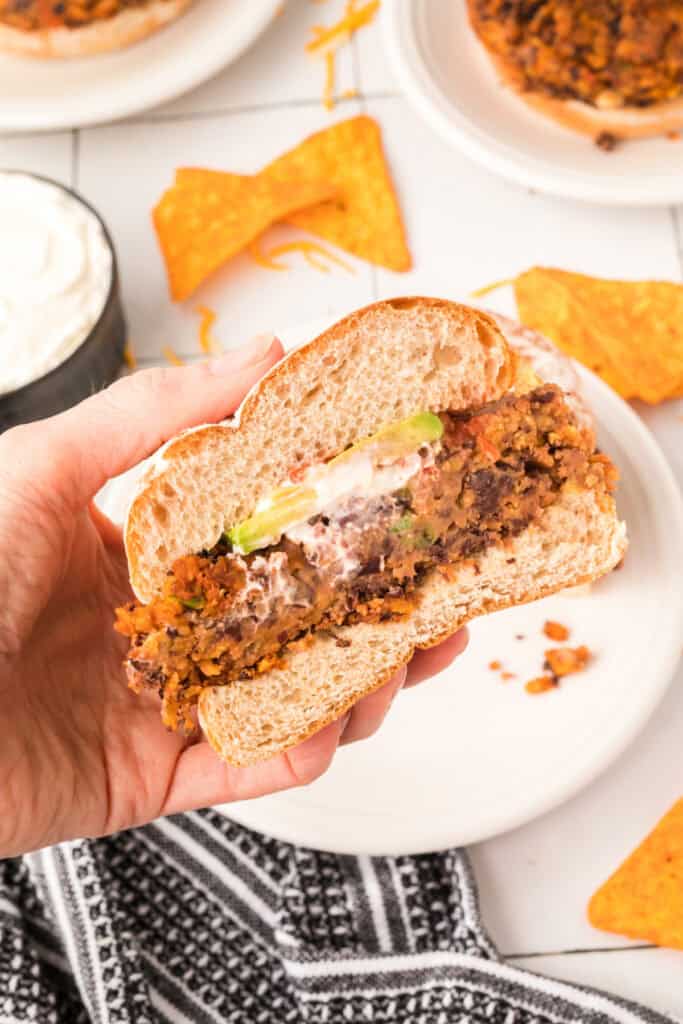 hand holding a cut Black Bean Nacho Burger showing the inside with avocado and creamy topping