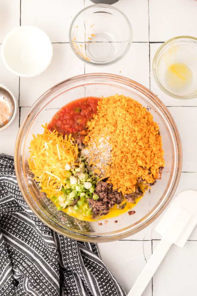 black bean mixture in a bowl with salsa, shredded cheese, crushed tortilla chips, and green onions added