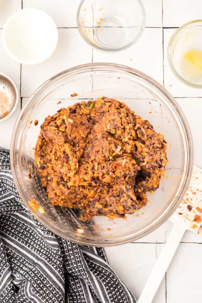 fully mixed black bean burger mixture in a glass bowl with visible cheese, beans, and chips
