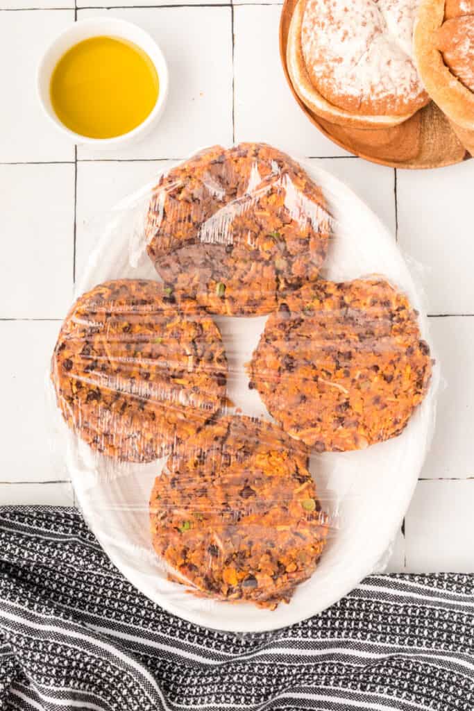 uncooked Black Bean Nacho Burger patties covered with plastic wrap on a plate