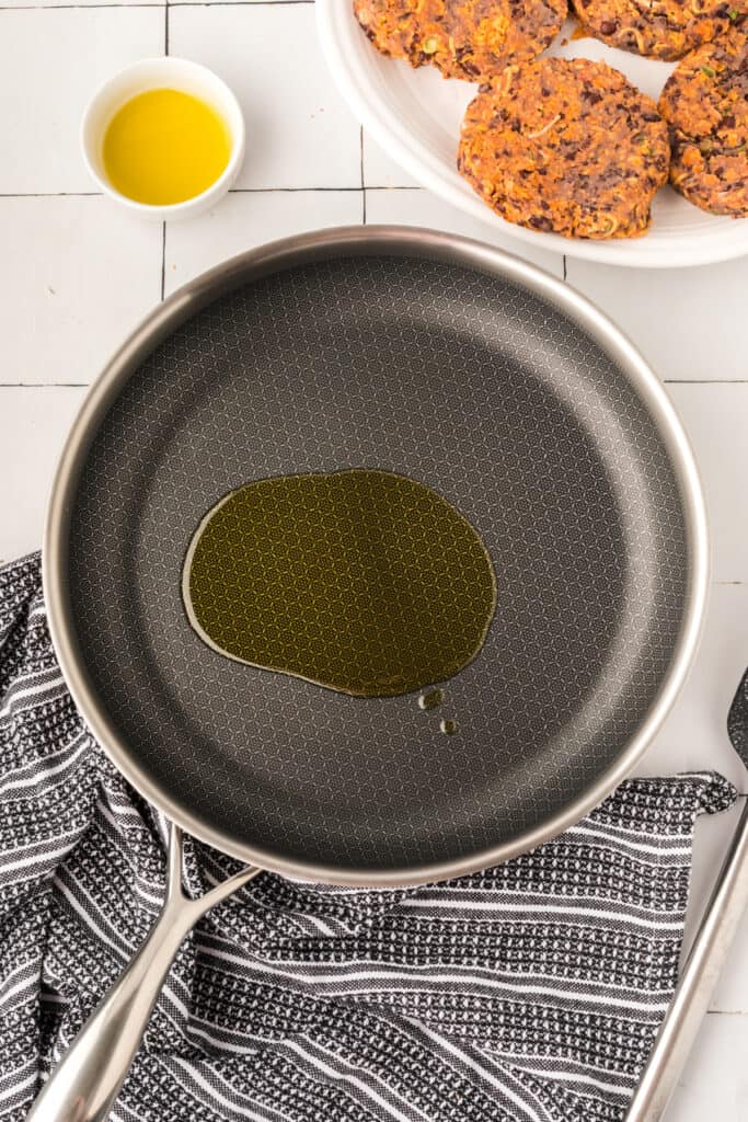 oil heating in a nonstick skillet with burger patties nearby ready to cook