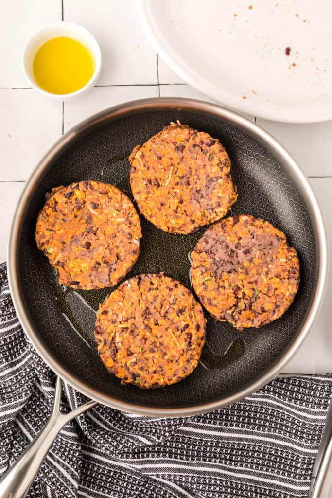Black Bean Nacho Burger patties cooking in a skillet with a crispy exterior forming