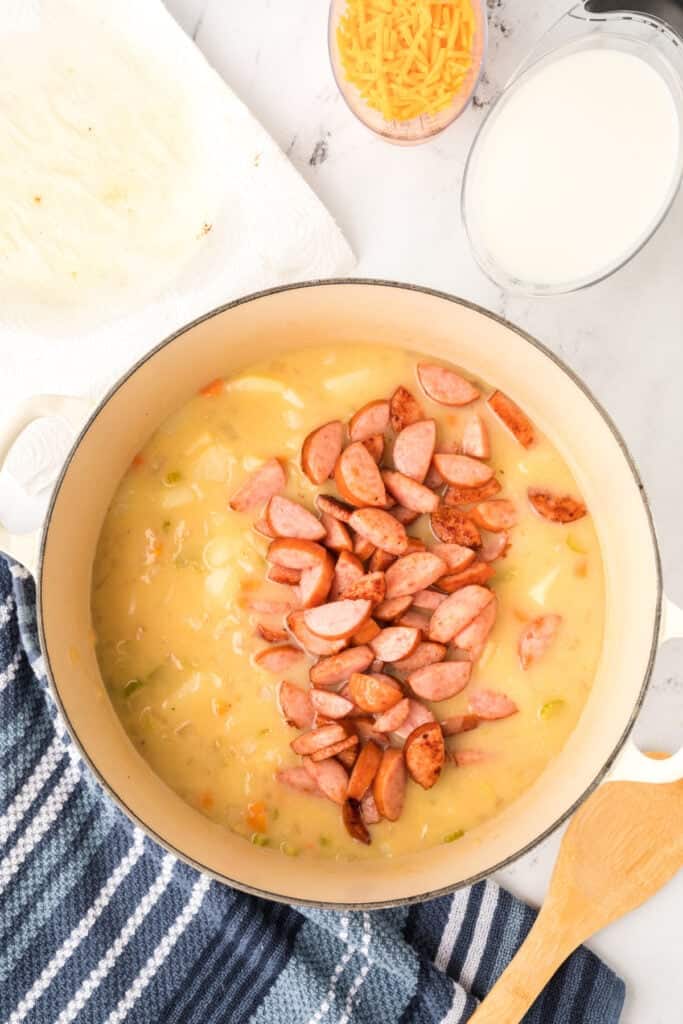 Cooked kielbasa sausage being added back into the pot of creamy potato soup.