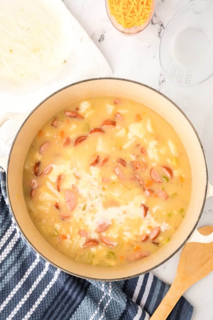 Milk poured into the pot of sausage and potato soup, creating a creamy base.