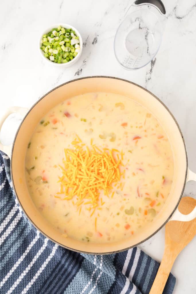 Shredded cheddar cheese sprinkled into the pot of creamy soup, ready to melt.