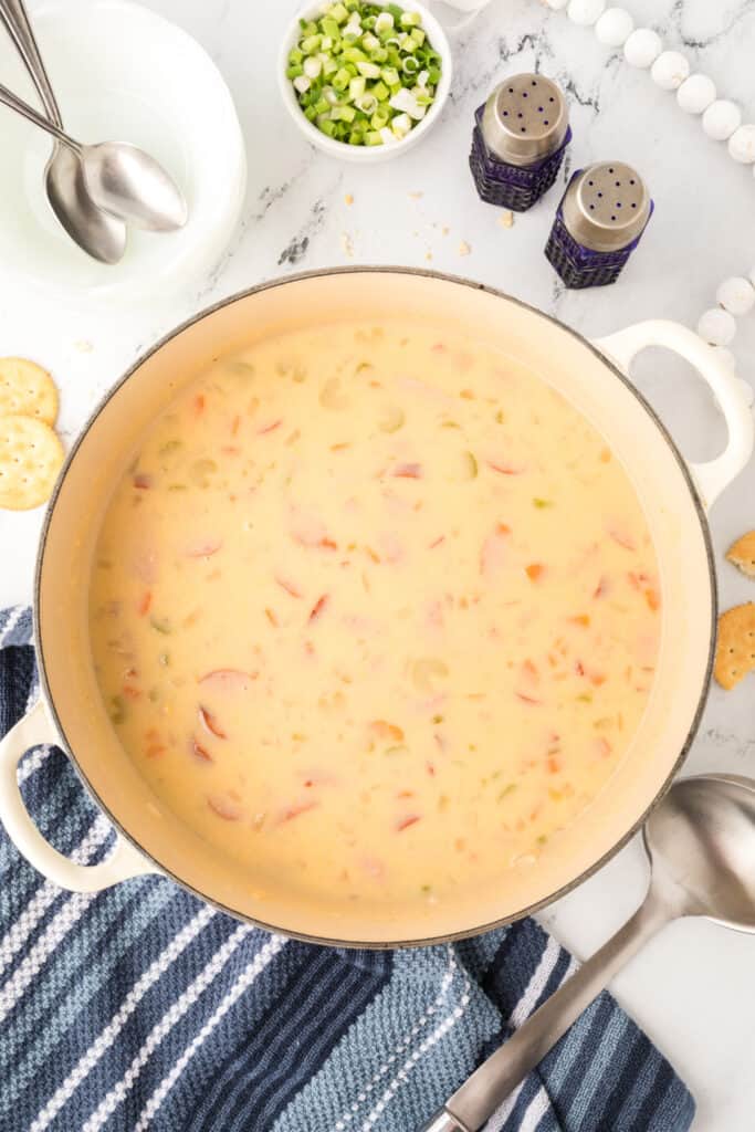 Finished pot of cheesy kielbasa potato soup with green onions and cheese nearby for garnish.