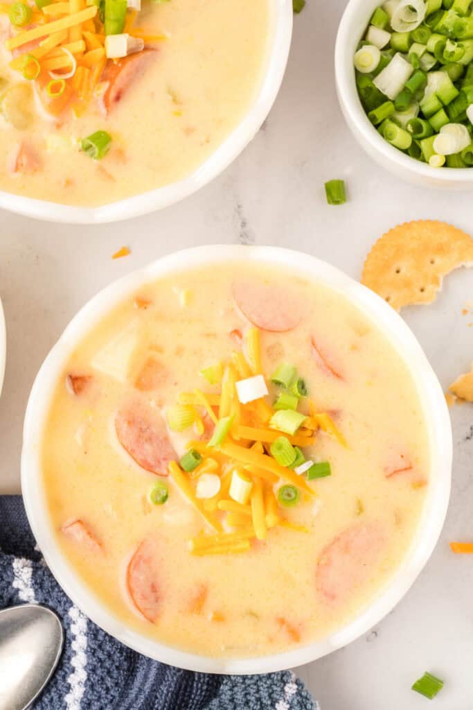 Overhead view of cheesy kielbasa potato soup in a large pot surrounded by bowls, crackers, and toppings.
