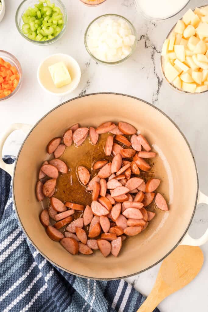 Browning kielbasa sausage pieces in a large pot with oil, giving them a golden color.