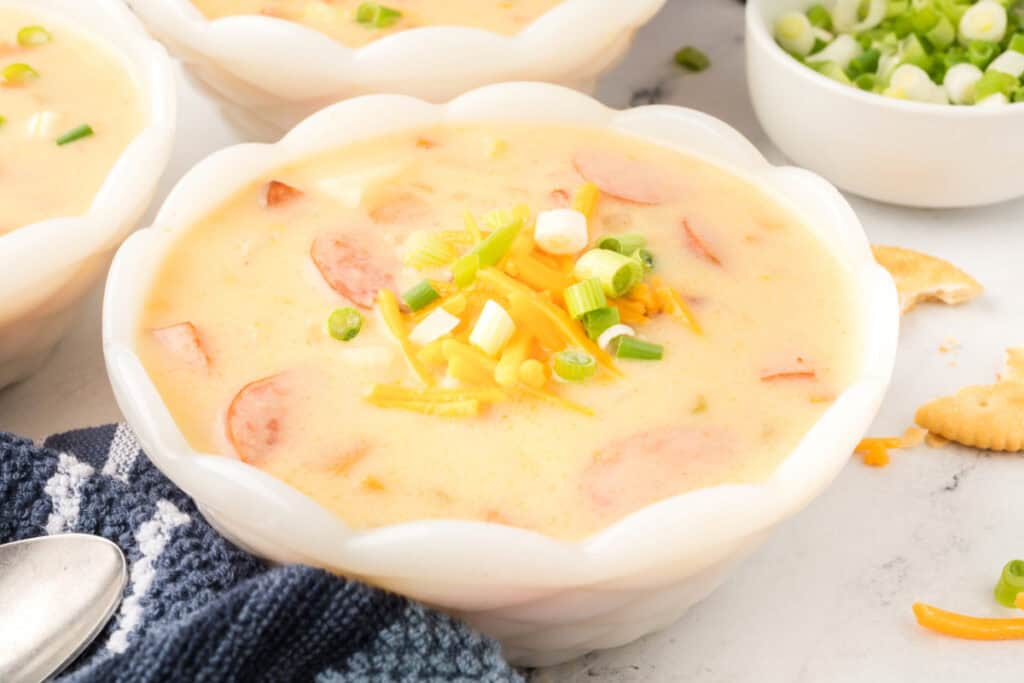 Close-up ladle full of cheesy kielbasa potato soup showing sausage slices, potatoes, and creamy broth.