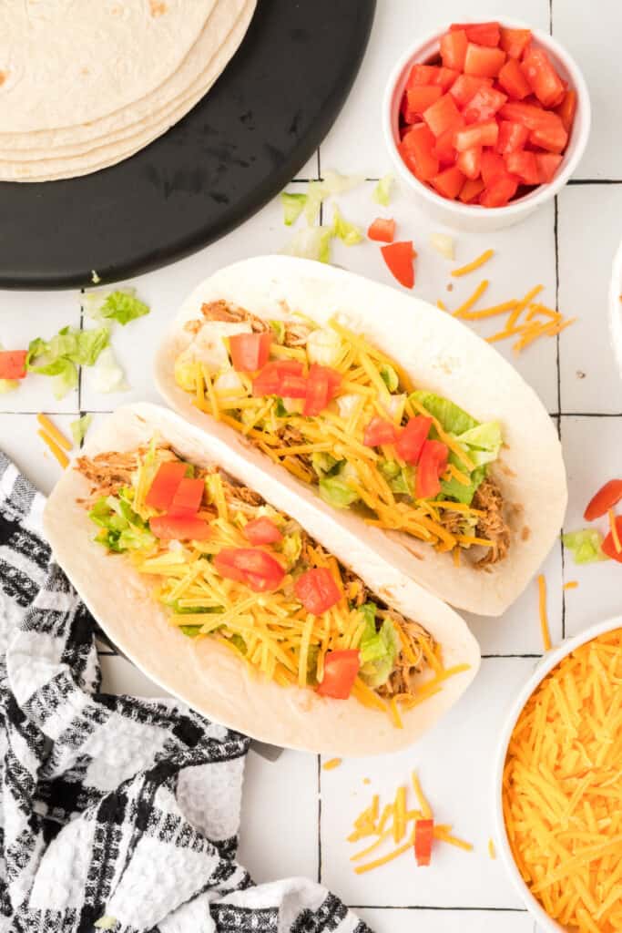 Two chipotle lime chicken tacos topped with lettuce, shredded cheese, and diced tomatoes