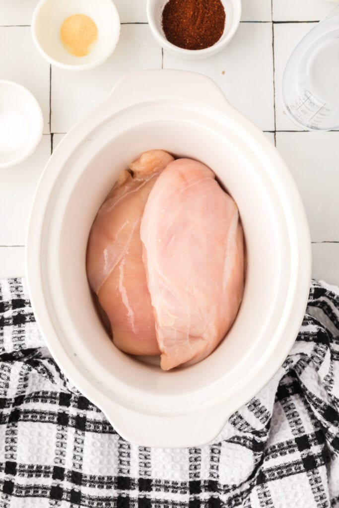 Raw chicken breasts placed in a slow cooker before seasoning