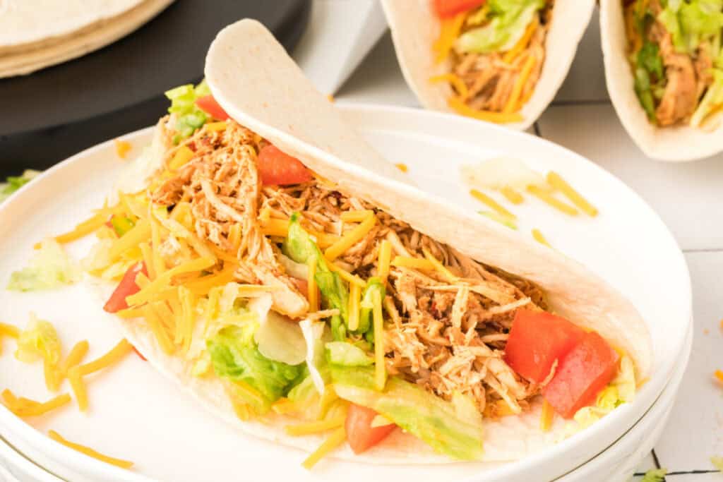Close-up of a chipotle lime chicken taco filled with shredded chicken, lettuce, cheese, and tomatoes