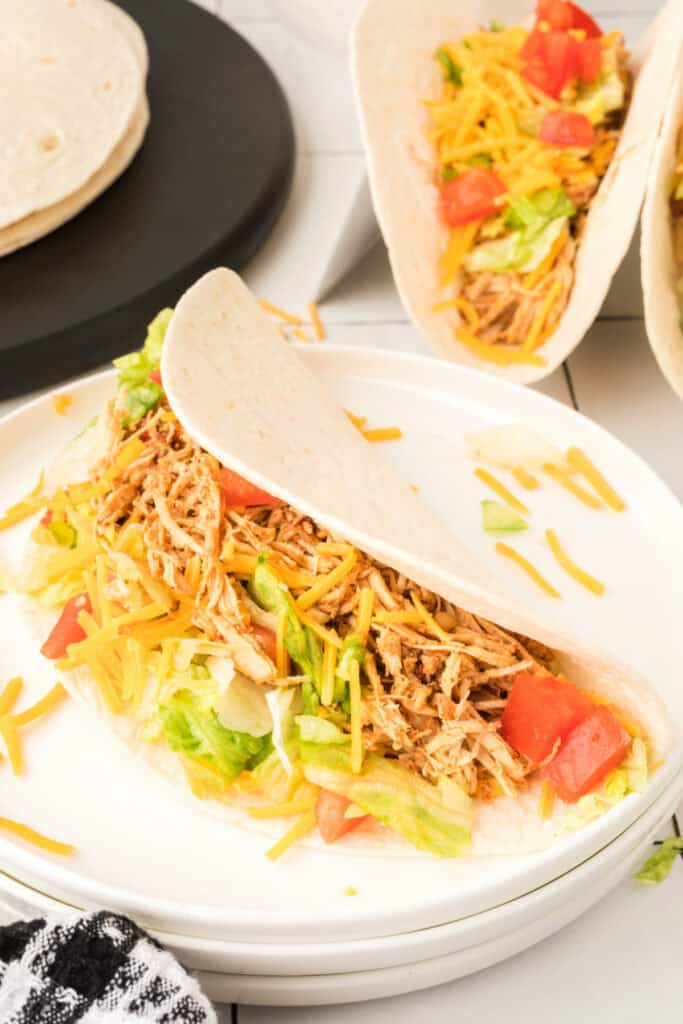 Chipotle lime chicken taco on a white plate with additional tacos in the background