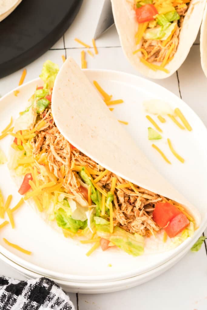 Side view of a chipotle lime chicken taco topped with shredded cheese, lettuce, and diced tomatoes