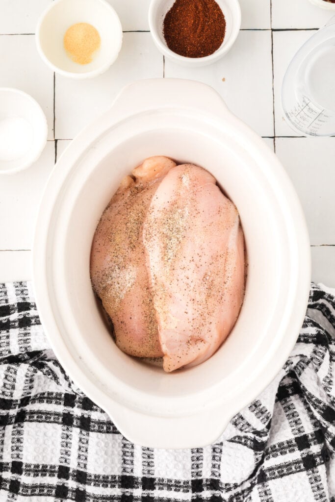 Raw chicken breasts in a slow cooker seasoned with salt, pepper, and garlic powder