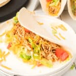 Chipotle lime chicken taco filled with shredded chicken, lettuce, cheddar cheese, and tomatoes on a white plate