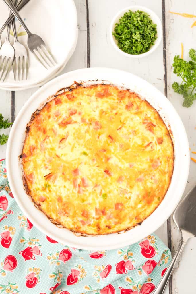 Fully baked Crustless Ham Bake in a white dish with golden brown edges and parsley on the side.