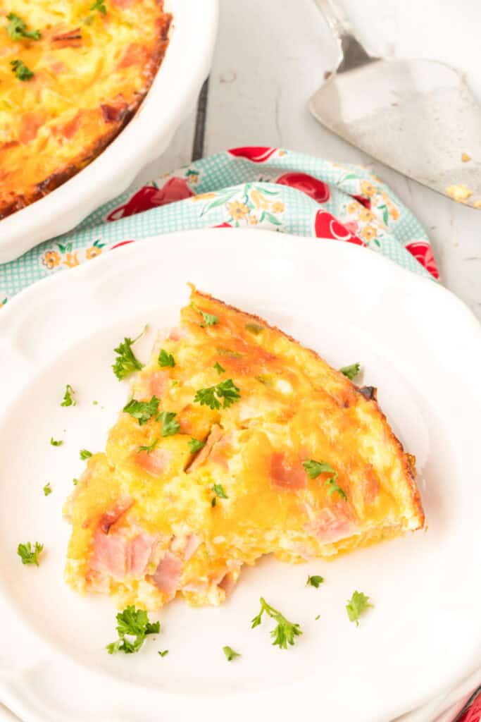 Slice of Crustless Ham Bake on a white plate garnished with fresh parsley.