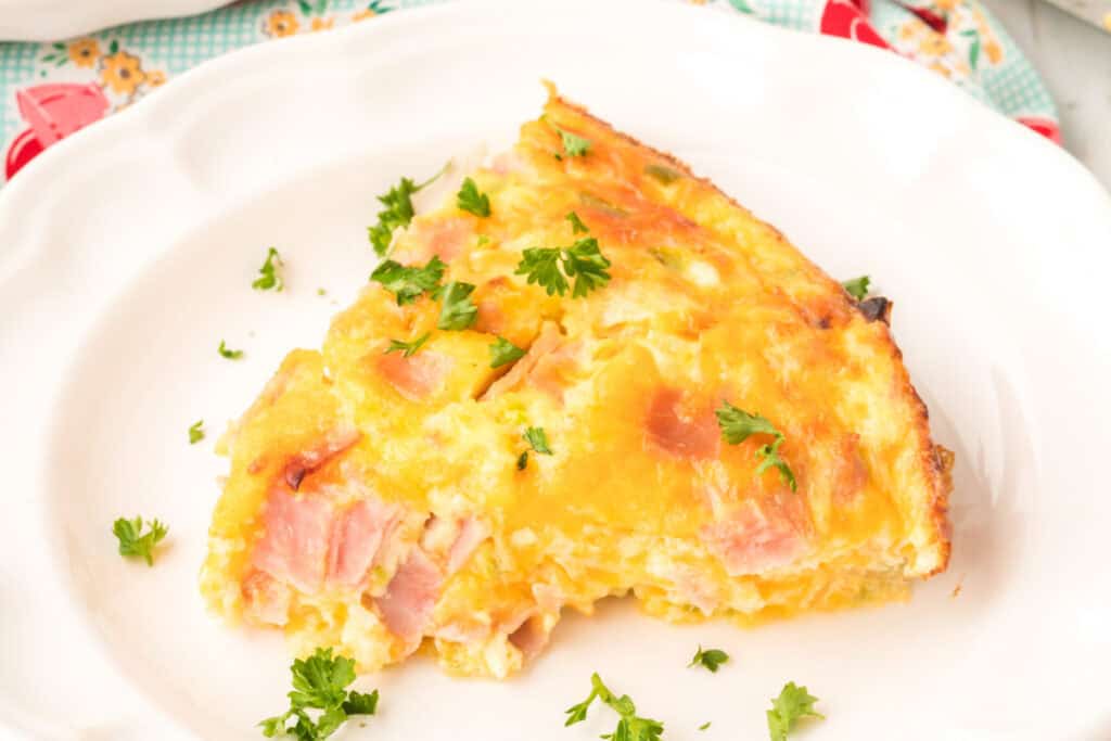 Close up of a slice of Crustless Ham Bake showing the layers of ham, cheese, and eggs with parsley.