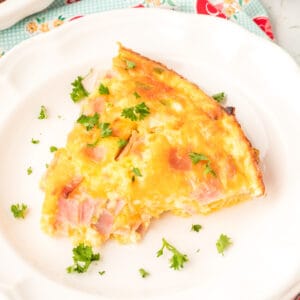 Overhead view of a slice of Crustless Ham Bake on a white plate topped with fresh parsley.