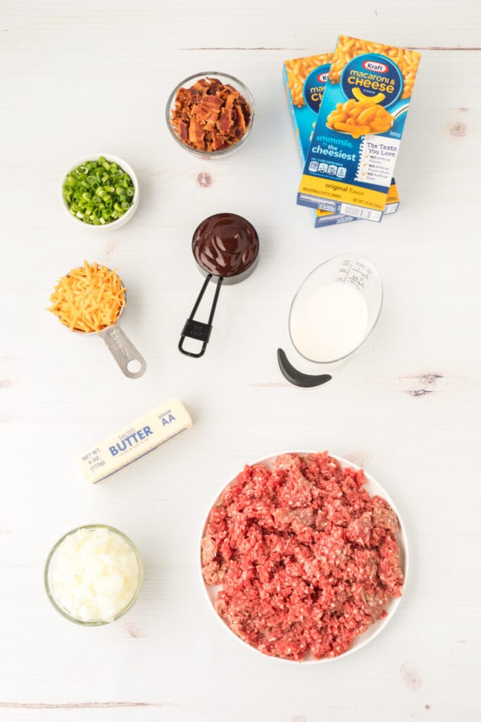 ingredients for BBQ Beefy Mac and Cheese including ground beef, bacon, boxed mac and cheese, cheddar cheese, BBQ sauce, milk, butter, onions, and green onions