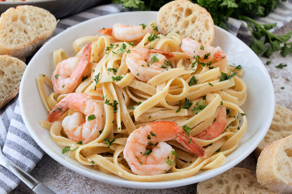 shrimp scampi pasta in white bowl with a slice of bread