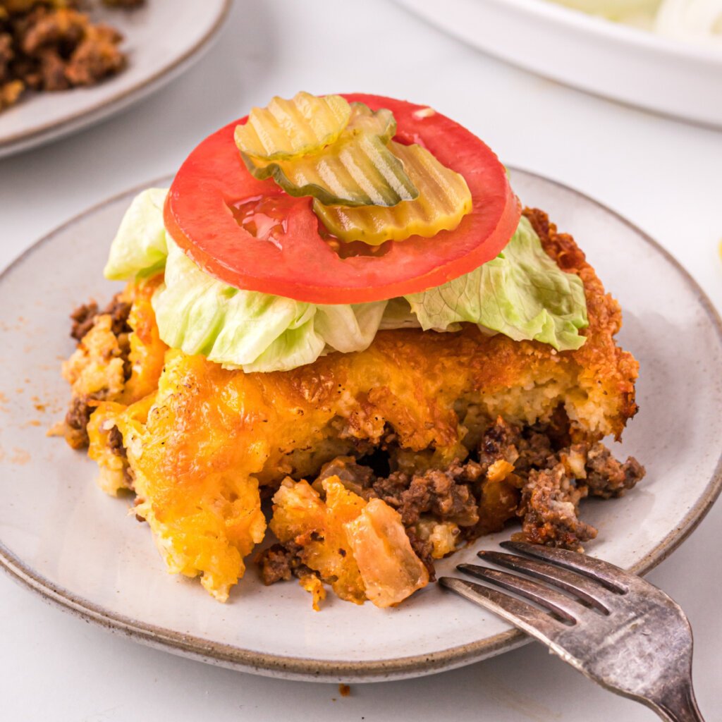 piece of cheeseburger casserole topped with lettuce tomato and pickles on a plate