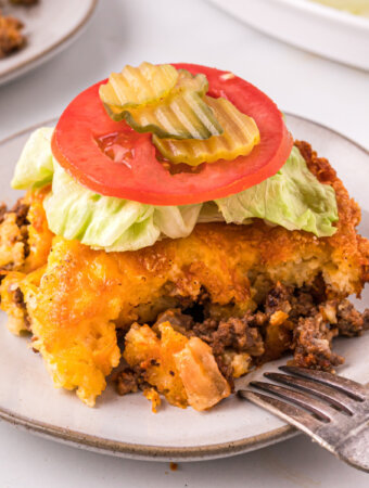 piece of cheeseburger casserole topped with lettuce tomato and pickles on a plate