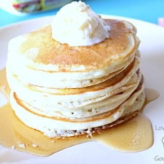 Pancakes stacked up on a plate with butter and syrup.